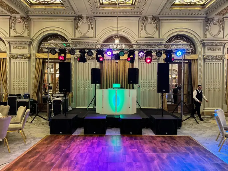 DJ setup cu booth luminat, sistem PA Electro-Voice (EV) și schelă de lumini moving heads într-o sală elegantă de evenimente