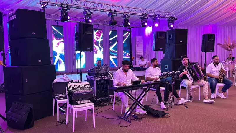 Formație live cu clape Korg, acordeon și saxofon cântând pe scenă cu ecrane LED verticale și sonorizare profesională