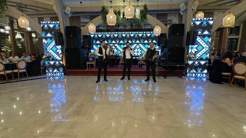 Formație live cu vioară și acordeon pe scenă, cu ecrane LED verticale afișând motive tradiționale și sistem PA