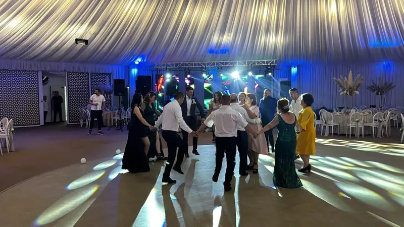Invitați dansând hora pe ringul de dans la nuntă/petrecere, cu lumini ambientale și scenă în fundal