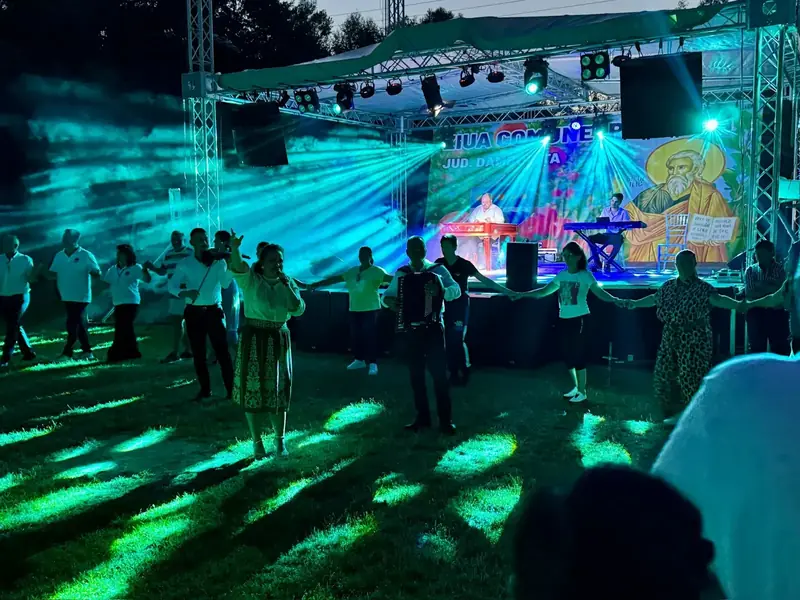 Public dansând hora la Ziua Comunei, cu lumini verzi laser și scenă în fundal
